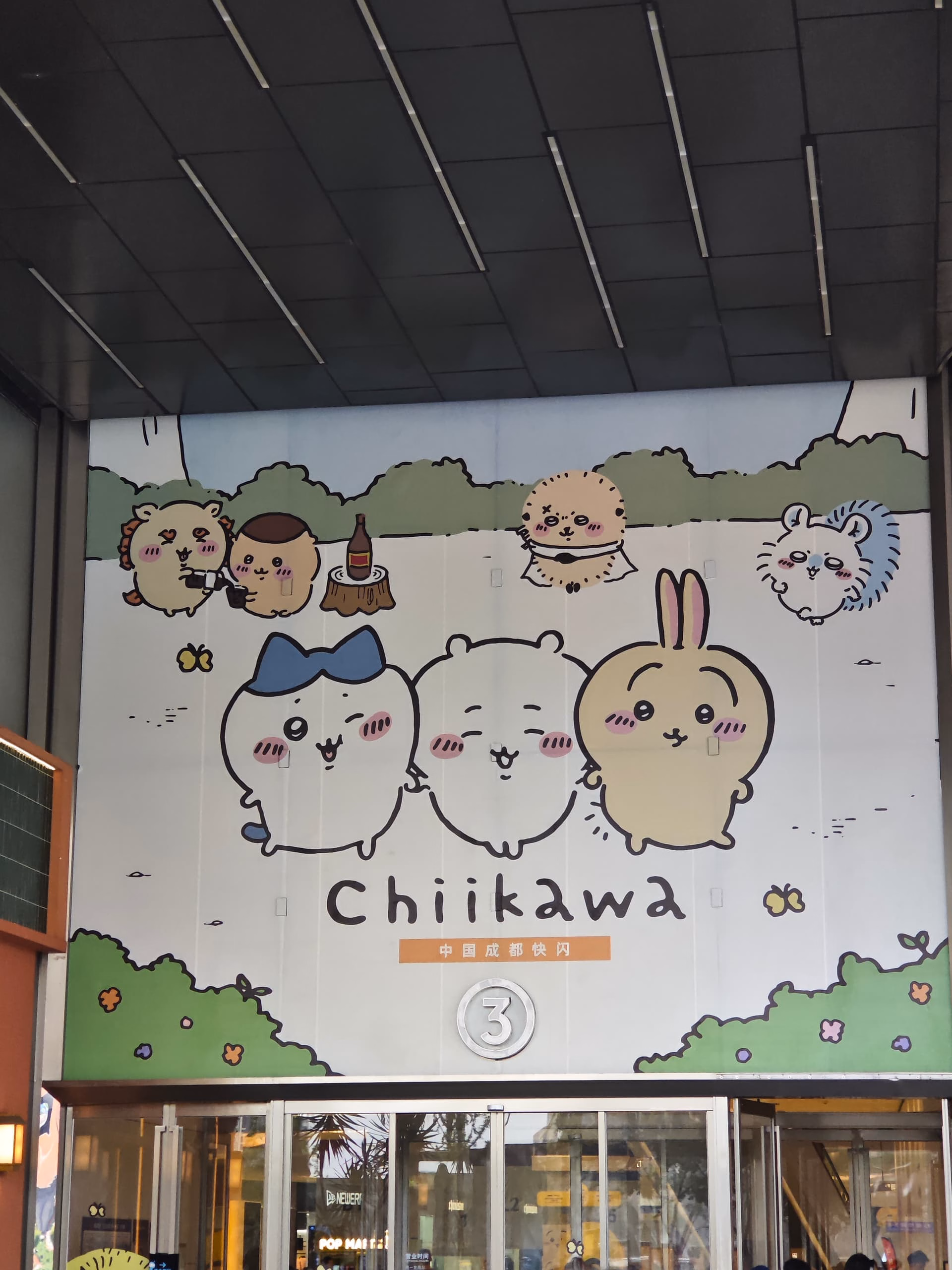 The image is a photo of a large sign featuring cartoon animals and the word "Chiikawa" in front of a building with glass doors and windows. (由 AI 生成标题)