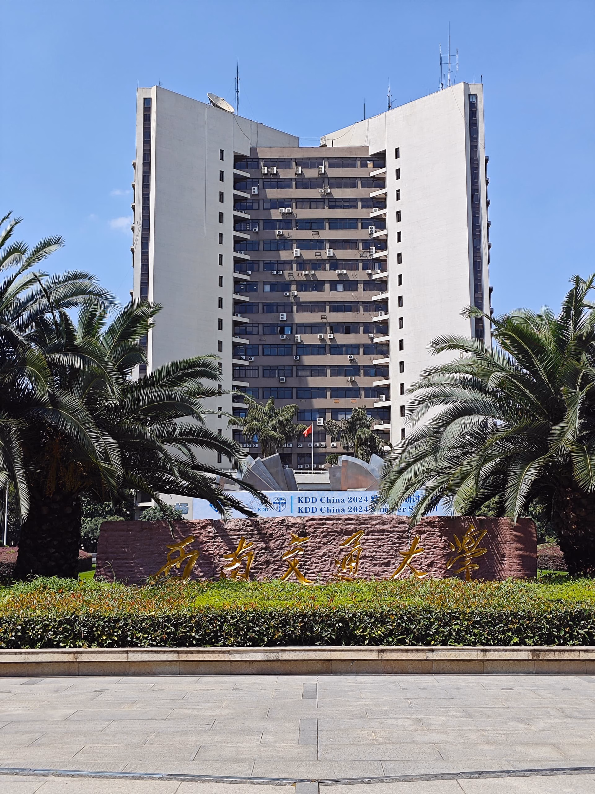The image shows a large, multi-story building with a sign and palm trees in front of it. (由 AI 生成标题)
