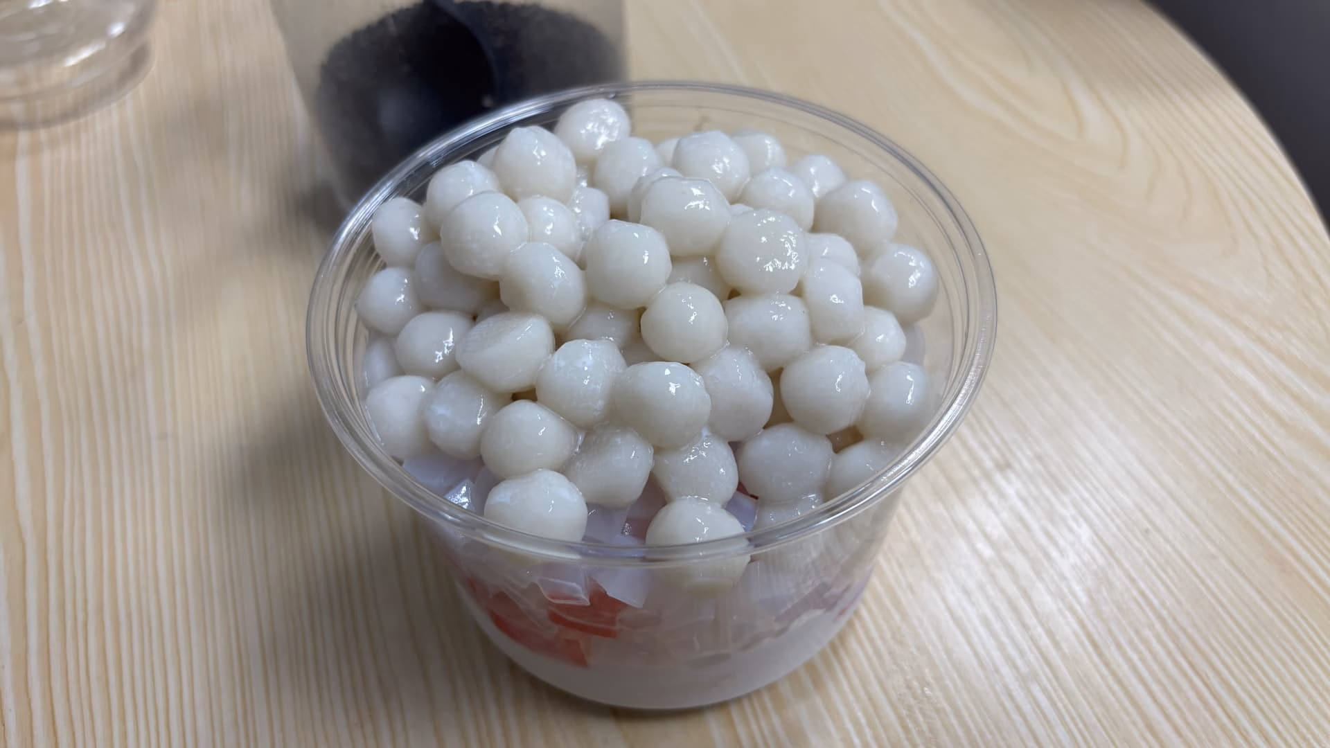 一张近距离的图片展示了一个装满白色汤圆的透明塑料杯。 (由 AI 生成标题)