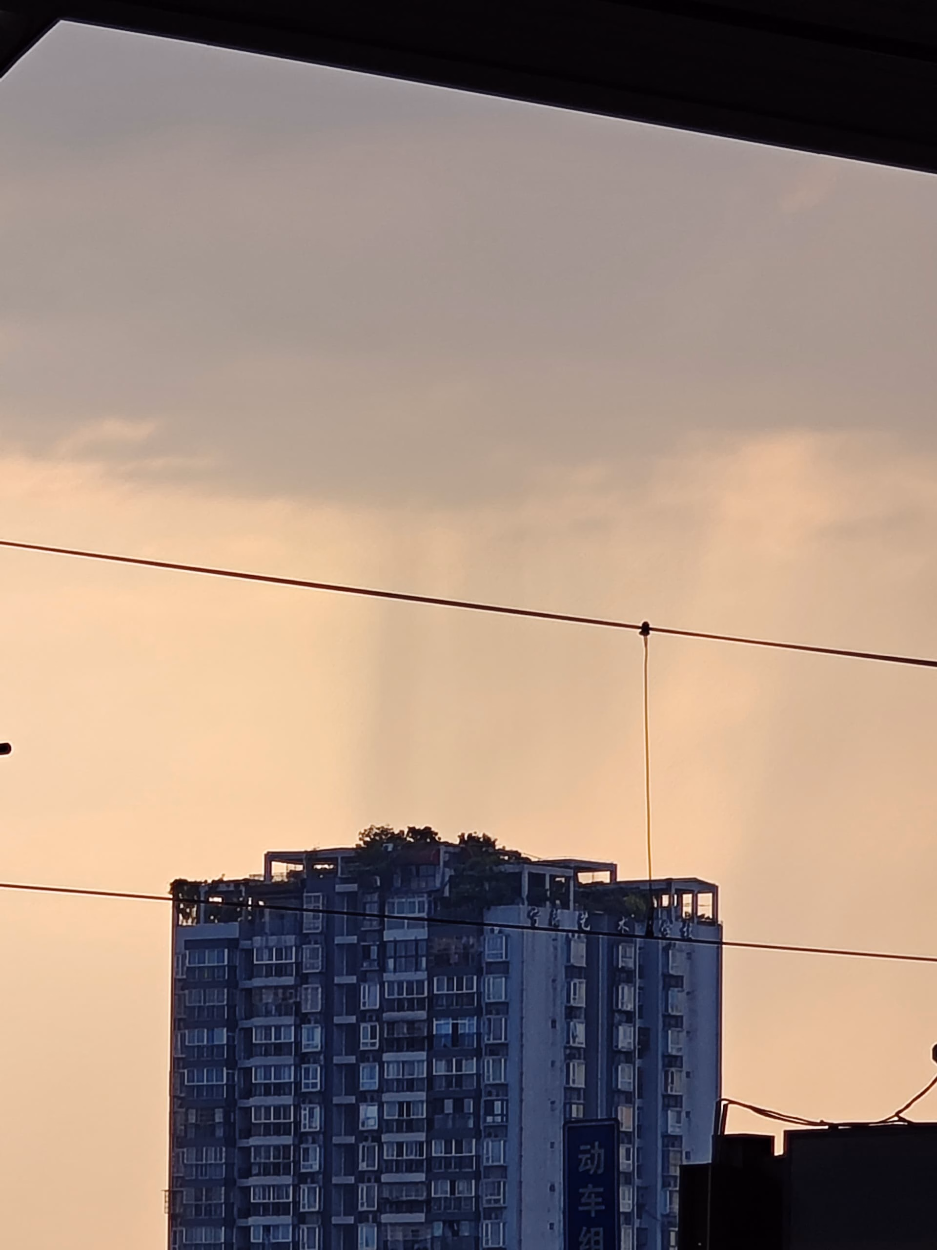 The image shows a tall building with many windows and balconies, set against a backdrop of a cloudy sky at sunset or sunrise. (由 AI 生成标题)
