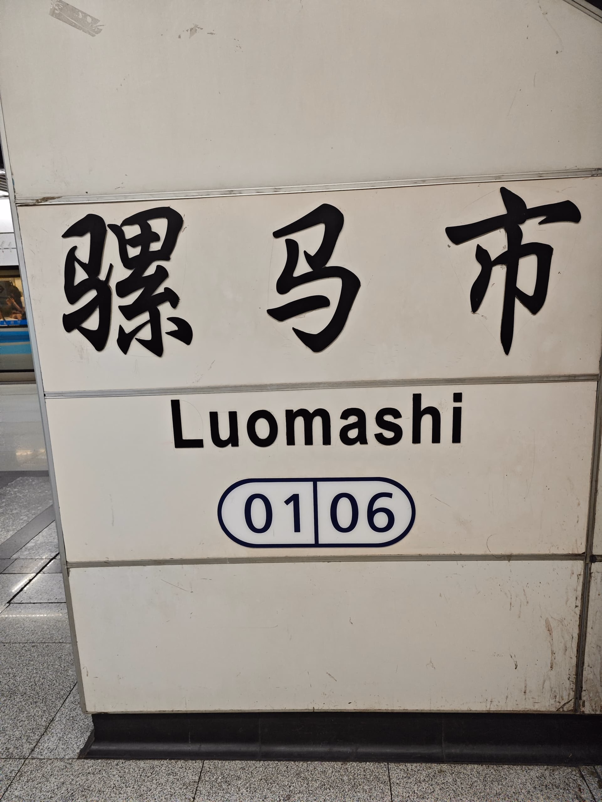 The image shows a sign with Chinese characters and English text, reading "Luomashi" and "01 06". (由 AI 生成标题)